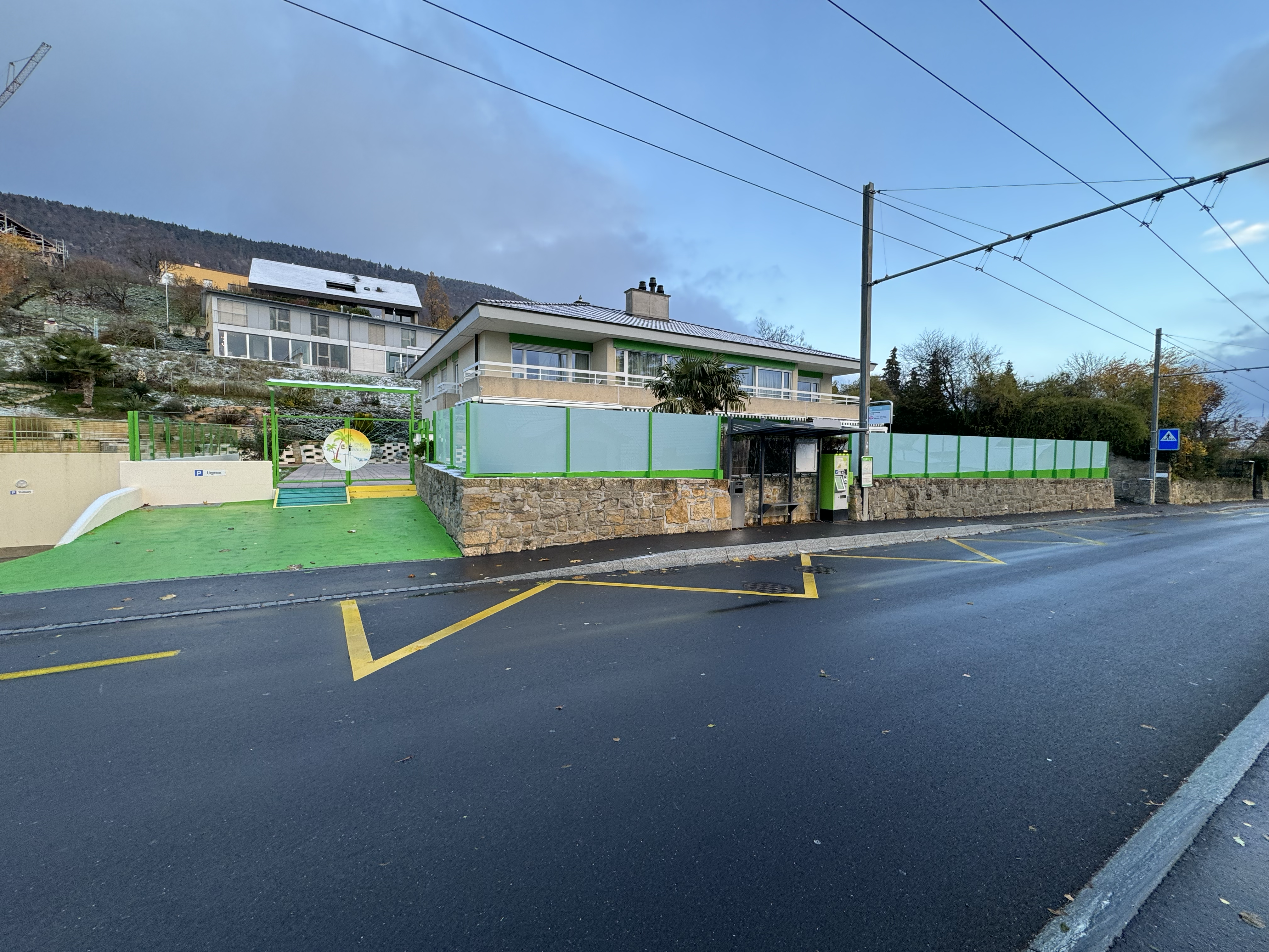 Building with green fencing and a bus stop next to yellow road markings.